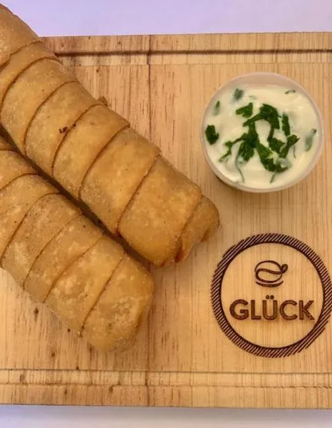 Tequeños Glück servidos sobre tabla de madera con salsa, listos para un evento